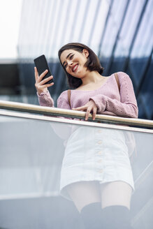 Lächelnde junge Frau schaut auf ihr Handy - JSMF00725