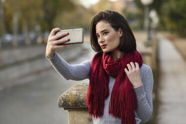 Porträt einer jungen Frau mit rotem Schal, die ein Selfie mit ihrem Handy macht - JSMF00734