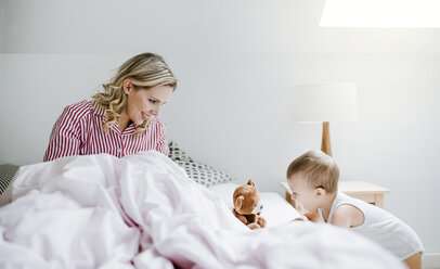 Smiling mother playing with toddler son in bed at home - HAPF02800