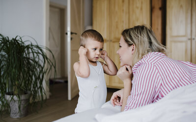 Lächelnde Mutter beobachtet Kleinkind Sohn mit Kopfhörer im Schlafzimmer zu Hause - HAPF02804