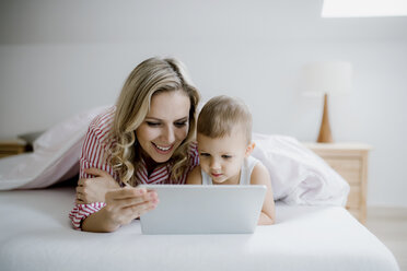 Lächelnde Mutter und Kleinkind Sohn im Bett liegend zu Hause mit Tablet - HAPF02809
