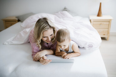 Lächelnde Mutter und Kleinkind Sohn im Bett liegend zu Hause mit Tablet - HAPF02810