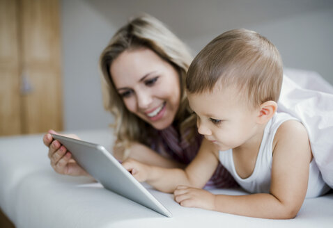 Lächelnde Mutter und Kleinkind Sohn im Bett liegend zu Hause mit Tablet - HAPF02811