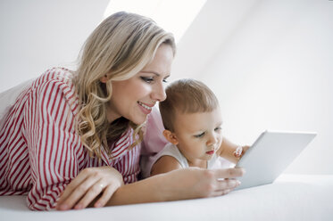 Smiling mother and toddler son lying in bed at home using tablet - HAPF02812