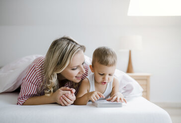 Lächelnde Mutter und Kleinkind Sohn im Bett zu Hause liegen und ein Buch lesen - HAPF02813