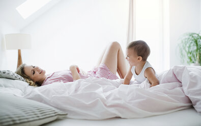 Smiling mother and toddler son lying in bed at home - HAPF02820