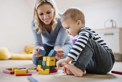 Lächelnde Mutter und ihr kleiner Sohn spielen mit Bauklötzen zu Hause, lizenzfreies Stockfoto