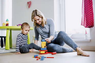 Smiling mother and toddler son playing with building blocks at home - HAPF02830