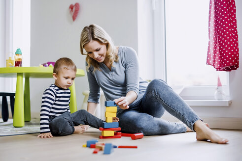 Lächelnde Mutter und ihr kleiner Sohn spielen mit Bauklötzen zu Hause - HAPF02830