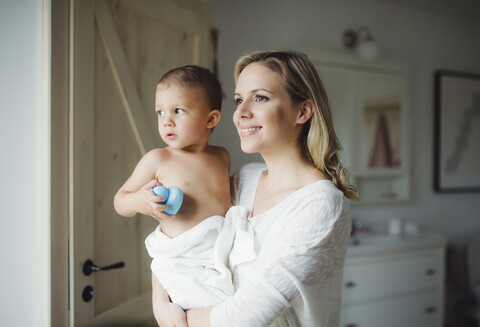 Lächelnde Mutter, die ihren kleinen Sohn im Badezimmer zu Hause hält, lizenzfreies Stockfoto