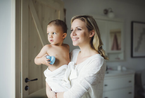 Lächelnde Mutter, die ihren kleinen Sohn im Badezimmer zu Hause hält - HAPF02840