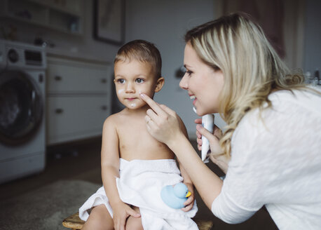 Lächelnde Mutter, die Hautcreme auf das Gesicht ihres kleinen Sohnes im Badezimmer zu Hause aufträgt - HAPF02841