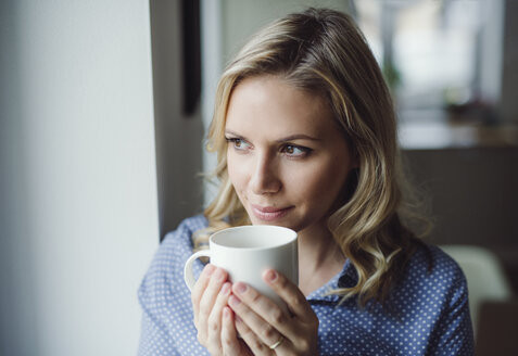 Lächelnde Frau mit einer Tasse Kaffee am Fenster zu Hause - HAPF02843