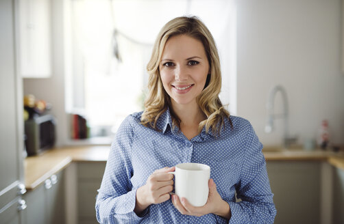 Porträt einer lächelnden Frau, die eine Tasse Kaffee zu Hause hält - HAPF02845