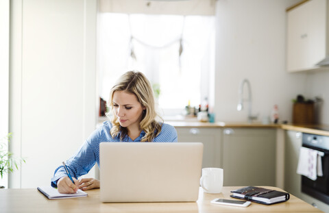 Woman with laptop working at home, taking notes stock photo