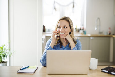 Lächelnde Frau mit Laptop und Mobiltelefon bei der Arbeit zu Hause - HAPF02854