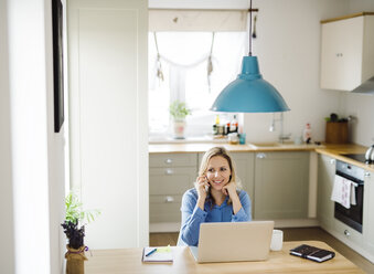 Smiling woman with laptop and cell phone working at home - HAPF02855