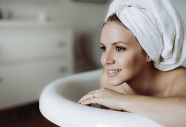 Lächelnde Frau mit Handtuch um den Kopf nimmt ein Bad zu Hause - HAPF02879
