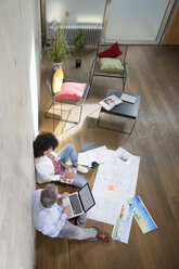 Businessman and businesswoman sitting on the floor in a loft working with laptop and documents - FKF03186