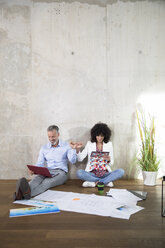 Geschäftsmann und Geschäftsfrau sitzen auf dem Boden in einem Loft und benutzen Laptop und Tablet - FKF03192