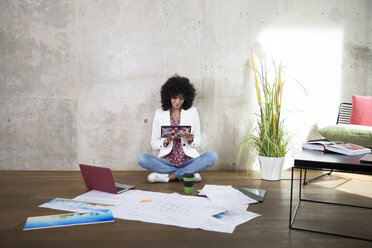 Businesswoman sitting on the floor in a loft using tablet - FKF03193