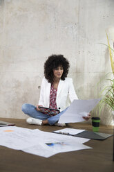Geschäftsfrau sitzt auf dem Boden in einem Loft und arbeitet mit Tablet und Dokumenten - FKF03194