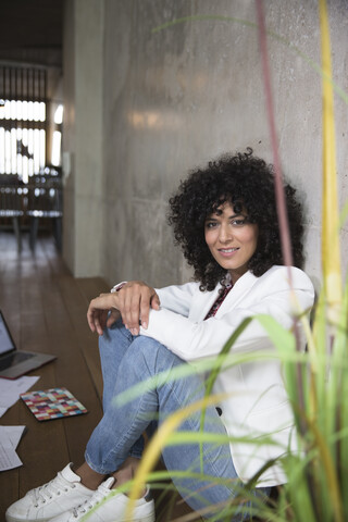 Portrait of smiling businesswoman sitting at concrete wall in a loft stock photo