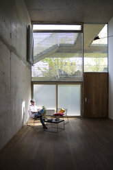 Businessman sitting in a loft at concrete wall having a break - FKF03209