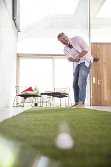 Glücklicher Geschäftsmann beim Golfspiel auf Kunstrasen in einem Loft - FKF03221