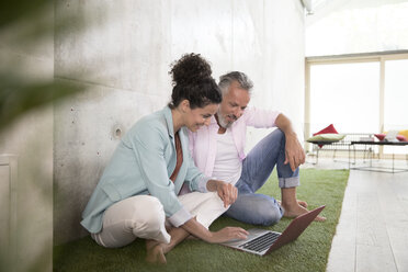 Casual businessman and businesswoman sitting on artificial turf in a loft sharing laptop - FKF03226