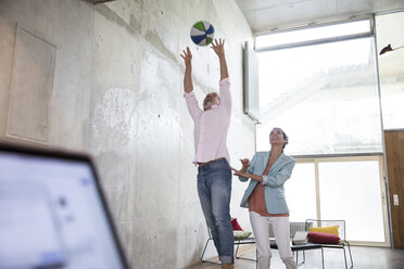 Glücklicher Geschäftsmann und Geschäftsfrau spielen Basketball in einem Loft - FKF03231