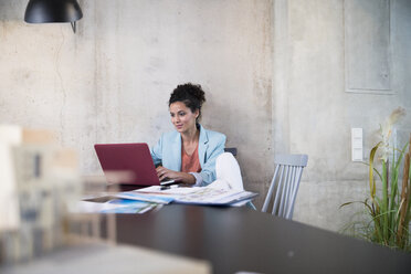 Businesswoman sitting at table in a loft using laptop - FKF03235