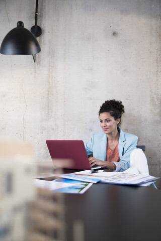 Geschäftsfrau sitzt am Tisch in einem Loft und benutzt einen Laptop, lizenzfreies Stockfoto