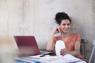 Portrait of smiling businesswoman sitting at table with documents and laptop - FKF03238