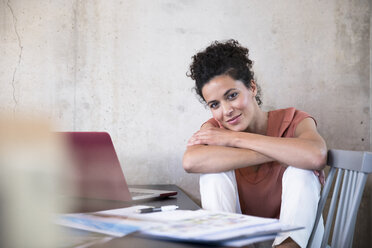 Portrait of smiling businesswoman sitting at table with documents and laptop - FKF03240