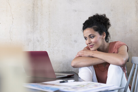 Lächelnde Geschäftsfrau sitzt am Tisch mit Dokumenten und Laptop, lizenzfreies Stockfoto