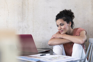 Smiling businesswoman sitting at table with documents and laptop - FKF03241