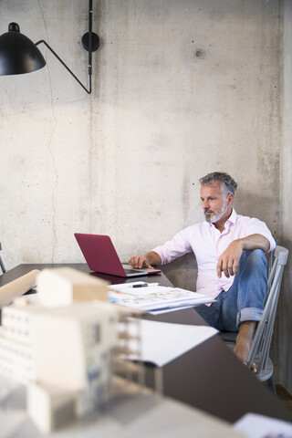 Geschäftsmann in einem Loft mit Laptop, Dokumenten und Architekturmodell auf dem Tisch, lizenzfreies Stockfoto