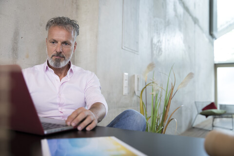 Geschäftsmann sitzt am Tisch in einem Loft und benutzt einen Laptop, lizenzfreies Stockfoto