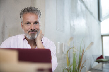 Portrait of confident businessman in a loft using laptop - FKF03252