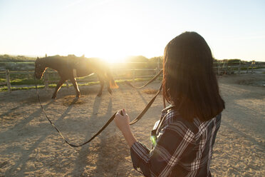 Spain, Tarifa, woman leading horse on riding ring at sunset - KBF00386