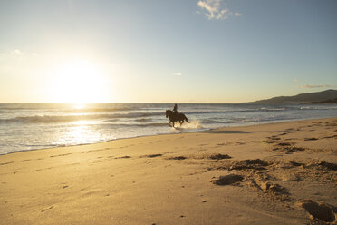 Spanien, Tarifa, Frau reitet Pferd am Strand bei Sonnenuntergang - KBF00388