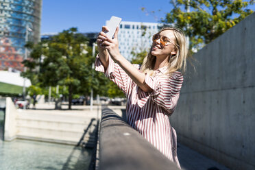 Spain, Barcelona, smiling young woman taking selfie with cell phone - GIOF05454