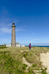 Denmark, Jutland, Skagen, Grenen, woman standing in dunes at grey lighthouse - UMF00897
