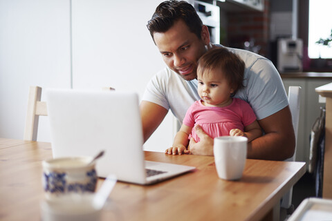 Vater mit kleinem Mädchen benutzt Laptop auf dem Tisch zu Hause, lizenzfreies Stockfoto