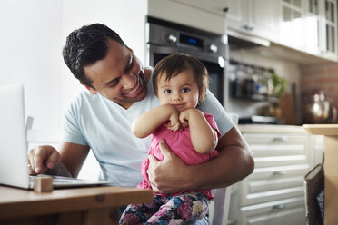 Smiling father with baby girl using laptop on table at home - ABIF01087