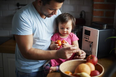 Father and baby girl eating fruit in kitchen at home - ABIF01089