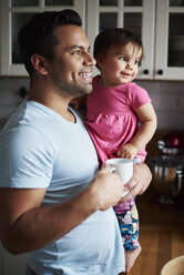 Smiling father holding baby girl in kitchen at home - ABIF01090