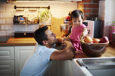 Smiling father looking at baby girl sitting on counter in kitchen at home - ABIF01093