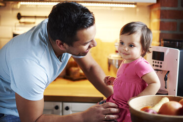 Smiling father looking at baby girl sitting on counter in kitchen at home - ABIF01095